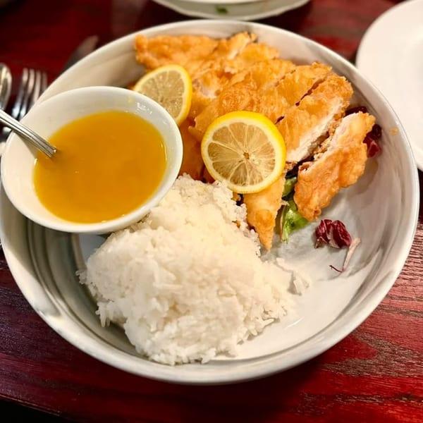 Crispy lemon chicken with white rice and a side of lemon sauce on a white plate.