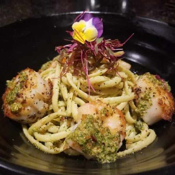 Scallops and pasta with pesto sauce, garnished with microgreens and an edible flower.