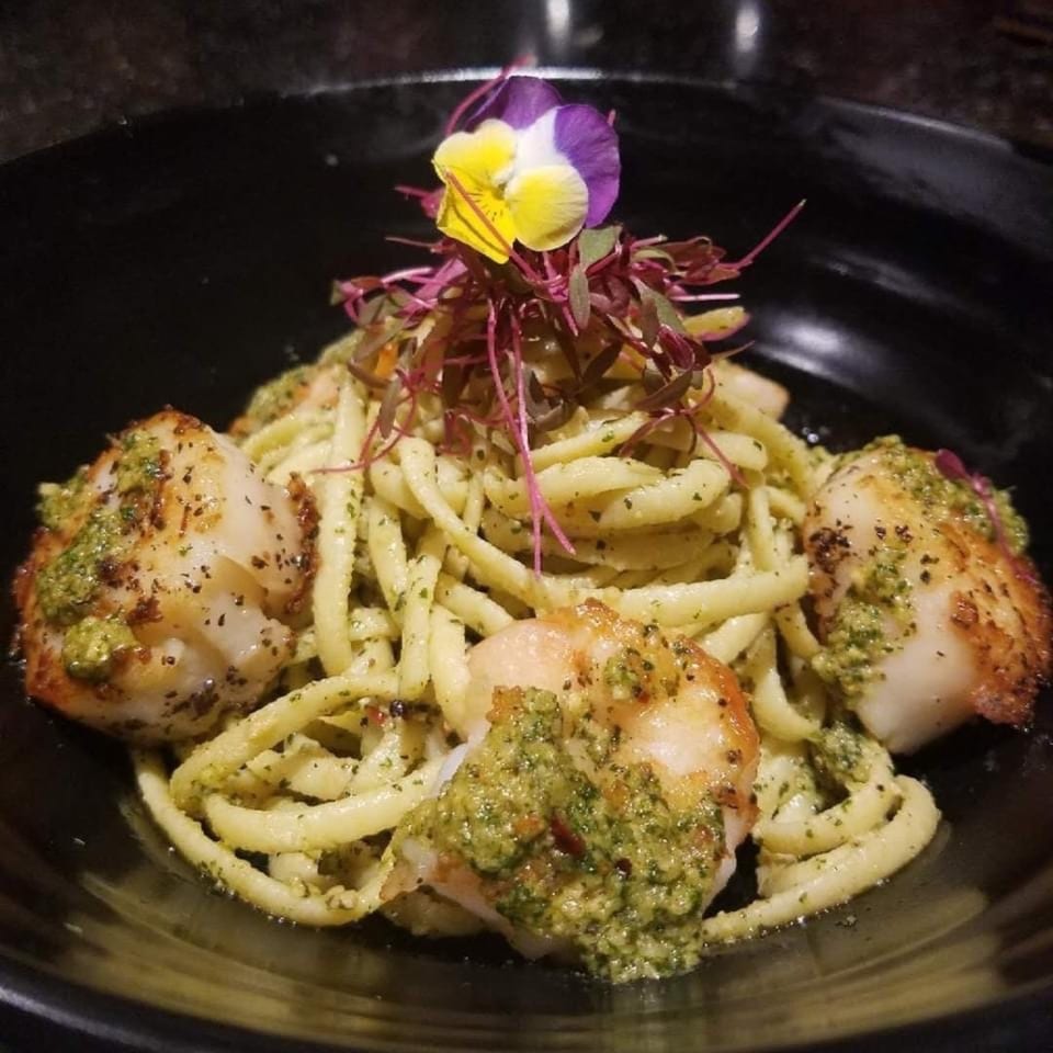 Scallops and pasta with pesto sauce, garnished with microgreens and an edible flower.