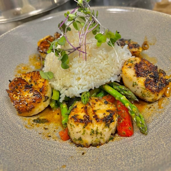 Seared scallops with white rice, asparagus, and red peppers on a gray plate.