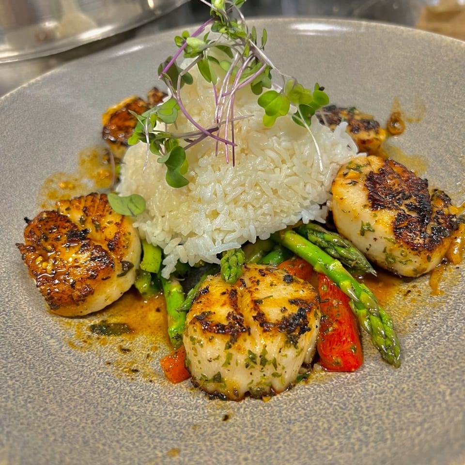 Seared scallops with white rice, asparagus, and red peppers on a gray plate.
